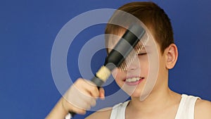 Portrait of an attractive caucasian boy 8 years old combing his hair and singing in front of a bathroom mirror. The child washes a
