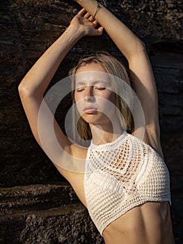 Portrait of attractive Caucasian woman wearing white top. Sexy woman standing near the rock on the beach. Tanned skin. Summer