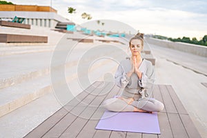 Portrait of attractive Caucasian young woman practicing yoga performing namaste pose with closed eyes outside in city