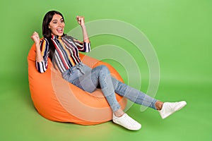 Portrait of attractive cheerful amazed girl lying in soft bag chair having fun rejoicing isolated over bright green