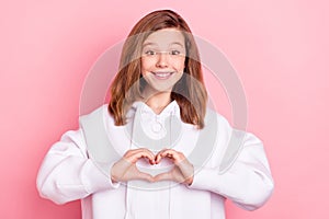 Portrait of attractive cheerful amorous girl showing heart shape figure isolated over pink pastel color background