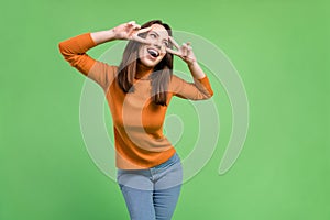 Portrait of attractive cheerful carefree pretty girl having fun showing double v-sign clubbing isolated over green color