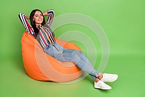 Portrait of attractive cheerful dreamy girl lying in soft bag chair resting isolated over green pastel color background