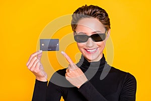 Portrait of attractive cheerful girl demonstrating card spend bugdet isolated over bright yellow color background