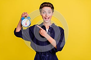 Portrait of attractive cheerful girl demonstrating retro clock isolated over bright yellow color background