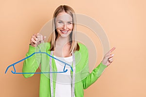 Portrait of attractive cheerful girl designer holding hanger demonstrating copy space isolated over beige pastel color