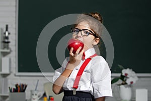 Portrait of attractive cheerful girl eating healthy food apple in class at elementary school.
