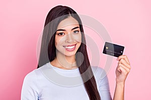 Portrait of attractive cheerful girl holding bank card order paypass technology isolated over pink pastel color