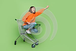 Portrait of attractive cheerful girl riding cart basket striving travel super hero isolated over bright green color