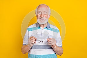 Portrait of attractive cheerful grey haired intellectual man holding in hands specs isolated over bright yellow color