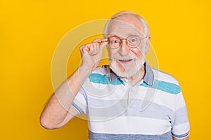 Portrait of attractive cheerful grey haired intelligent man touching specs isolated over bright yellow color background