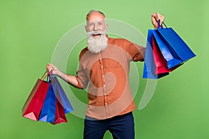 Portrait of attractive cheerful grey-haired man holding buyings having fun store retail isolated over green color photo