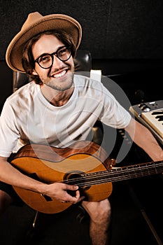 Portrait of attractive cheerful man happily playing on a guitar recording new song in music studio