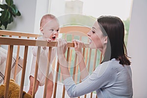 Portrait of attractive cheerful mum having a baby in crib talking new life spending free time at home flat indoors