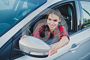 Portrait of attractive cheerful wavy-haired girl driving car fixing mirror spending time rest vacation trip tour