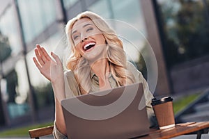 Portrait of attractive cheerful wavy haired girl using netbook waving hi hello waiting friend in complex outdoors