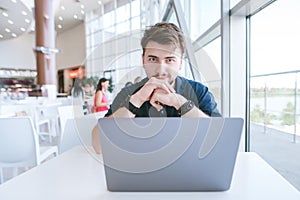 Portrait of an attractive chelovek who is sitting with a laptop in a cafe and looking into the camera