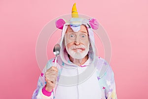 Portrait of attractive comic hungry grey-haired man holding spoon grimacing isolated over pink color background