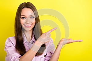 Portrait of attractive confident cheerful girl holding on palm demonstrating copy space ad isolated over bright yellow