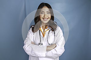 Portrait of an attractive confident female doctor, friendly smiling arms crossed wear white lab coat stethoscope isolated blue