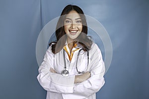 Portrait of an attractive confident female doctor, friendly smiling arms crossed wear white lab coat stethoscope isolated blue