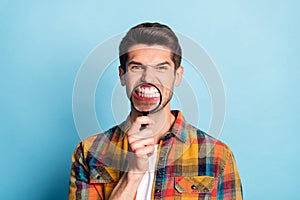 Portrait of attractive crazy funky dangerous guy holding in hand enlarge glass evil teeth  over bright blue