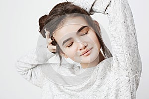 Portrait of attractive cute european girl with tender smile and closed eyes stretching tired muscles while touching hair
