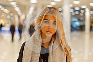 Portrait of an attractive cute young blonde woman with sexy lips with beautiful gray eyes in a coat in a vintage scarf indoors.