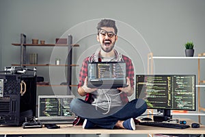 Portrait of attractive desperate crazy guy hacker sitting on table holding laptop code database at work place station