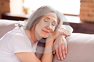 Portrait of attractive dreamy calm grey-haired woman granny sitting on divan resting free time at home house flat