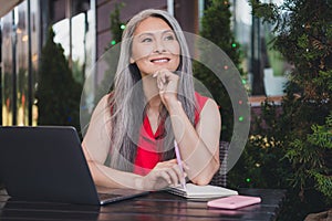 Portrait of attractive dreamy cheerful grey-haired woman using laptop fantasizing realestate agent broker outdoors