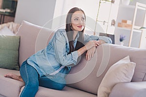 Portrait of attractive dreamy cheerful woman sitting on divan resting fantasizing at home indoors
