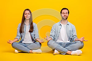 Portrait of attractive dreamy couple sitting meditating om zen isolated over bright yellow color background