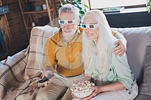 Portrait of attractive elderly cheerful couple sitting on sofa hugging having fun watching tv at loft industrial