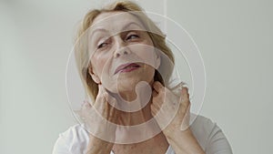 Portrait of an attractive elderly woman holding two hands on her neck
