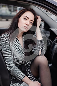 portrait of attractive fabulous brunette woman wearing checkered dress in a lux car. lady in automobile.