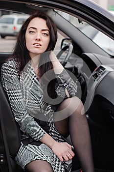 portrait of attractive fabulous brunette woman wearing checkered dress in a lux car. lady in automobile.