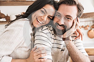 Portrait of attractive family man and woman 30s wearing aprons cooking in kitchen at home