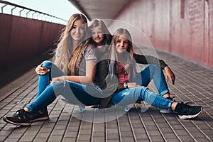 Portrait of an attractive family. Mother and her daughters sitting together on a skateboard at bridge footway.