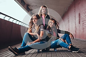 Portrait of an attractive family. Mother and her daughters sitting together on a skateboard at bridge footway.