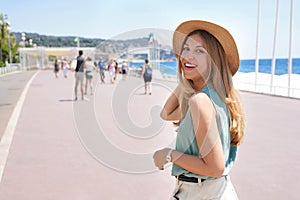 Portrait of attractive fashion woman turns around and smiling at camera walking along Promenade des Anglais, Nice, France