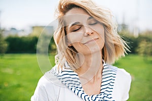 Portrait of attractive female with blond blowing hair and closed eyes enjoy weather. Close up shot of Caucasian beautiful young