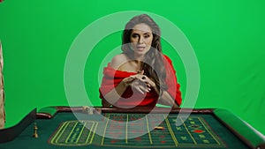 Portrait of attractive female on chroma key green screen. Woman in red dress at the roulette table with croupier makes