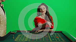 Portrait of attractive female on chroma key green screen. Woman in red dress sitting at the roulette table with croupier