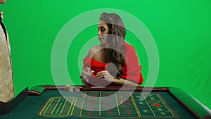 Portrait of attractive female on chroma key green screen. Woman in red dress sitting at the roulette table with croupier