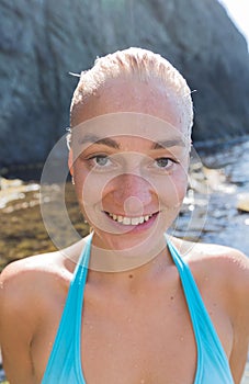 Portrait of attractive female person with wet slicked hair against rocky beach