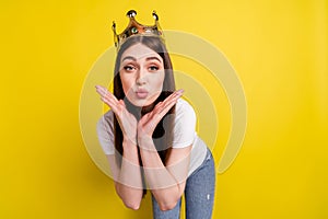 Portrait of attractive feminine amorous girl wearing crown sending you air kiss isolated over bright yellow color