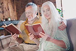 Portrait of attractive focused cheerful careful couple sitting on sofa hugging reading book at loft industrial interior
