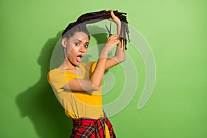 Portrait of attractive funky worried girl cutting curls problem solution  over bright green color background