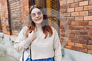 Portrait of attractive girl in good mood looks at camera. Modern lady in sunglasses posing in city. Happy woman on a